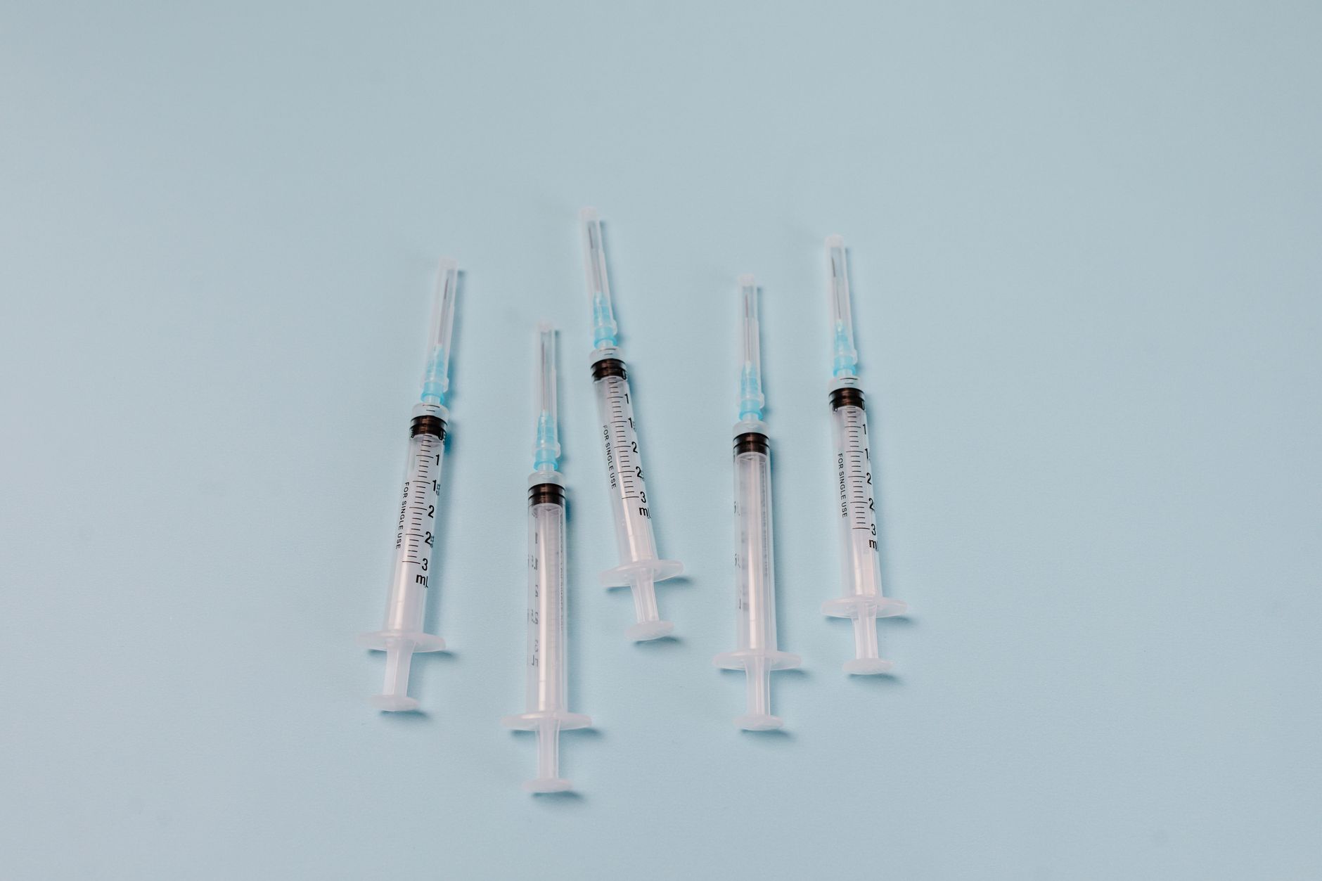 Close-up of sterile syringes arranged on a light blue surface, ideal for medical themes.
